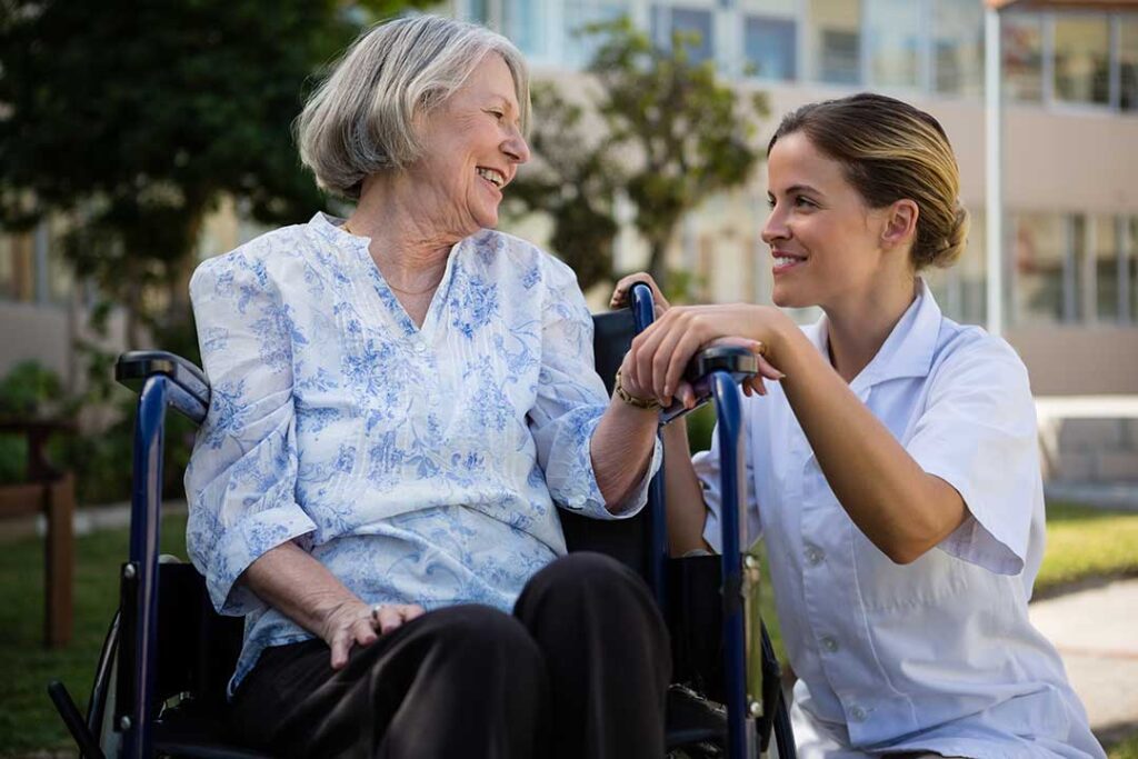 Older adults chatting together at a dining table in a bright assisted living community room.